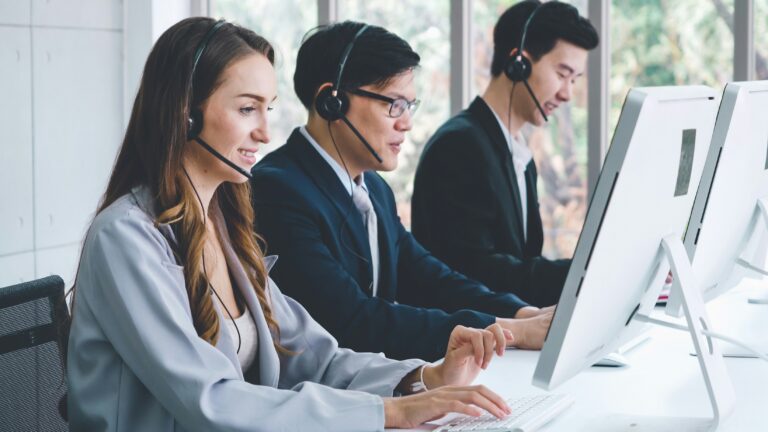 Three medical billing agents sit at a desk facing their computer screens.