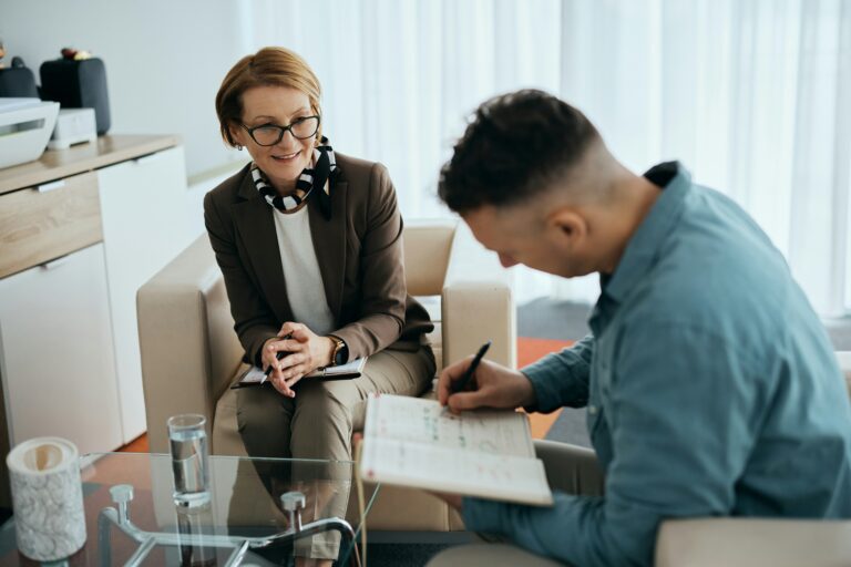 A psychiatrist smiles at her patient as he journals during their session in her office.