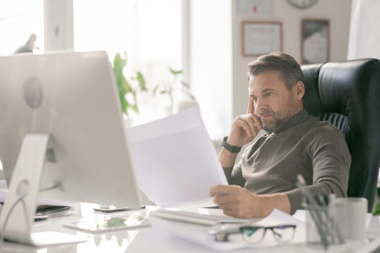 A man reads a document at his desk in an office.