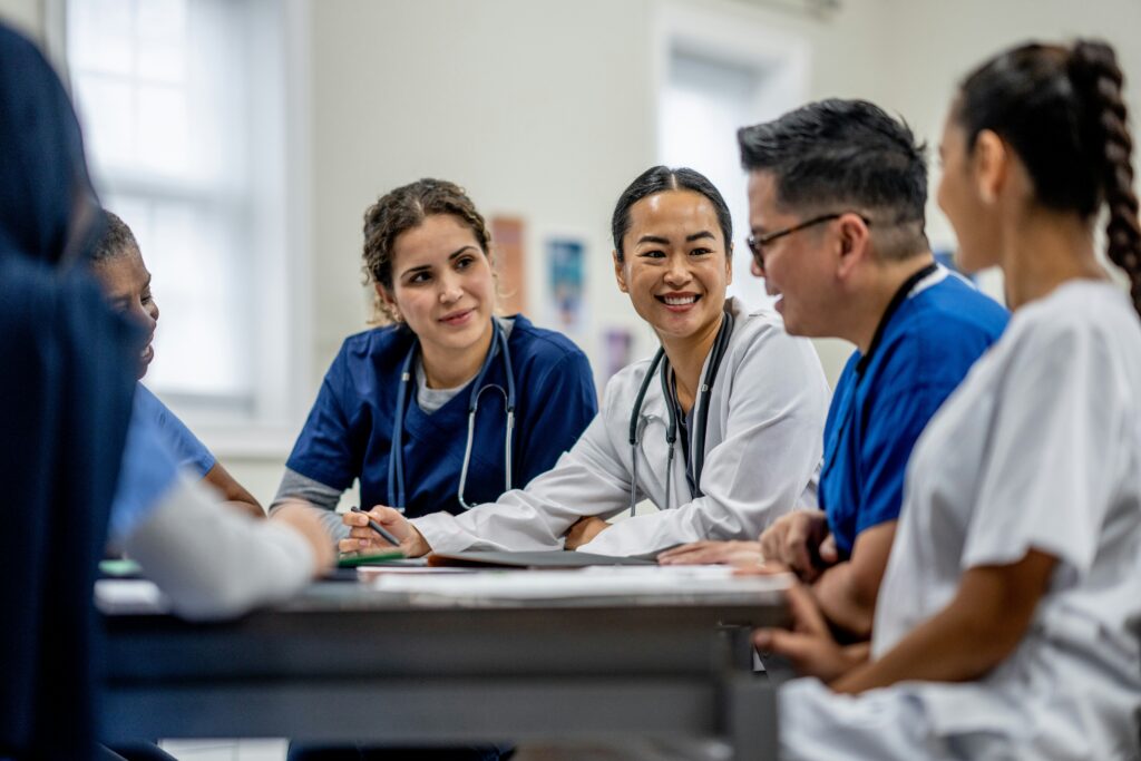 Five doctors smile around a table inside of an office.