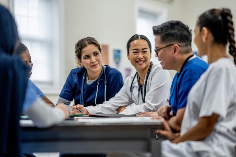 Five doctors smile around a table inside of an office.